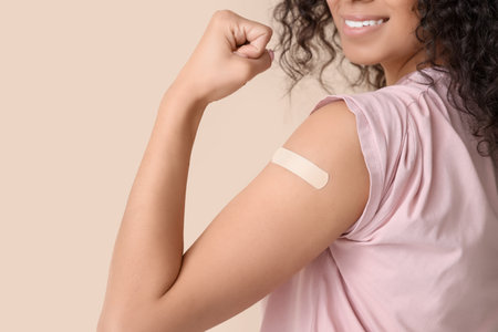 Young woman with medical patch showing muscles after vaccination on beige background, closeupの写真素材