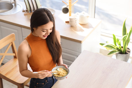 Young Asian woman eating tasty ramen in kitchenの写真素材