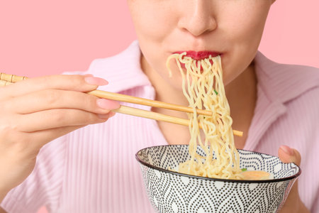 Young woman eating tasty ramen on pink background, closeupの写真素材