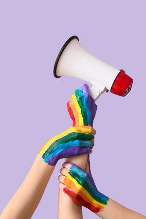 Female hands painted in colors of LGBT flag with megaphone on lilac backgroundの写真素材