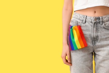 Woman with LGBT flag in her pocket of jeans on yellow background, closeup