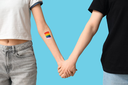 Women with drawn LGBT flag holding hands on blue backgroundの写真素材