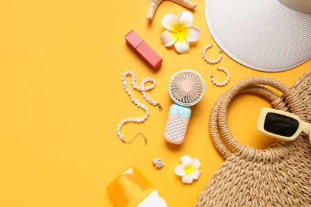 Bag with female summer accessories and mini fan on yellow background with space for text