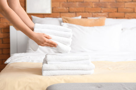 Young chambermaid stacking clean towels on bed in bedroom, closeupの写真素材