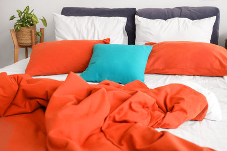Cozy bed with soft colorful pillows and crumpled blanket in bedroomの写真素材