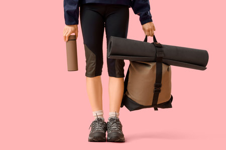 Female tourist with flask and backpack on pink background
