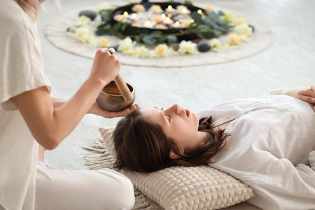 Healer with Tibetan singing bowl cleansing energy of young womanの写真素材