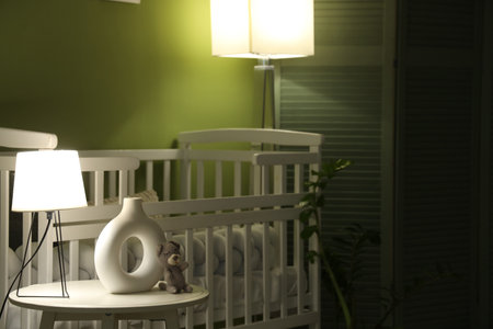 Interior of children's bedroom with baby crib, coffee table and glowing lamps near green wall at night, closeupの写真素材