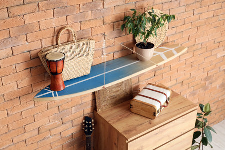 Surfboard with drum, bag and plant on brick wall in roomの写真素材