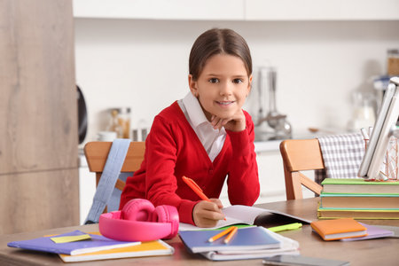 Cute schoolgirl doing homework at table in kitchenの写真素材