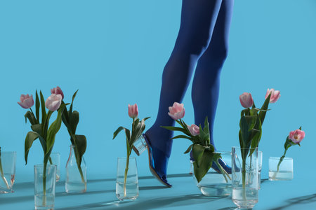 Legs of young woman in blue tights and glass vases with beautiful tulip flowers on color backgroundの写真素材