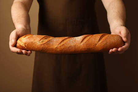 Man with fresh baguette on brown background, closeupの写真素材