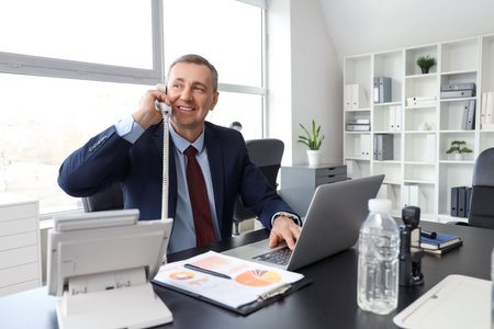 Portrait of handsome mature businessman talking by telephone at table in officeの写真素材