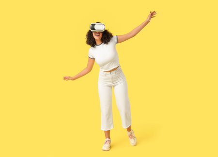 Young African-American woman with VR glasses on yellow background
