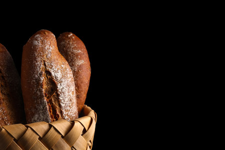 Wicker basket with fresh rye baguettes on black backgroundの写真素材