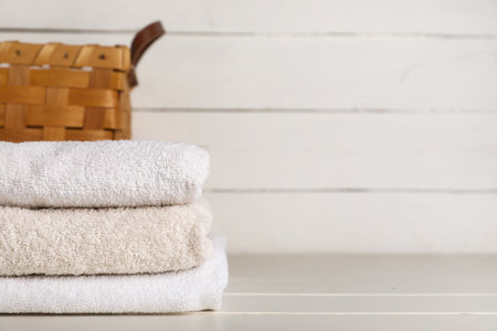 Stack of clean towels and wicker basket on light wooden tableの写真素材