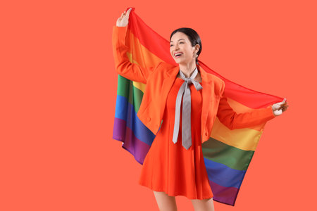Beautiful young woman with rainbow flag on orange background. LGBT conceptの写真素材