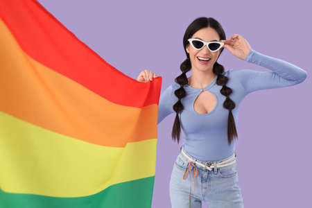 Beautiful young woman with rainbow flag on lilac background. LGBT conceptの写真素材