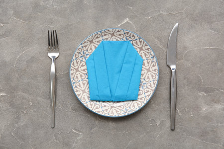 Plate with cutlery and origami from paper napkin on gray grunge backgroundの写真素材