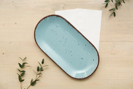 Plate with paper napkins and eucalyptus on wooden background