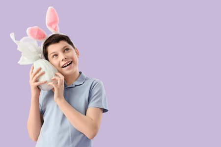 Teenage boy in bunny ears with Easter gift egg on lilac background