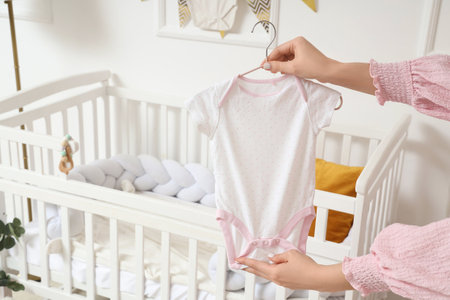 Young woman with baby bodysuit in nursery, closeupの写真素材