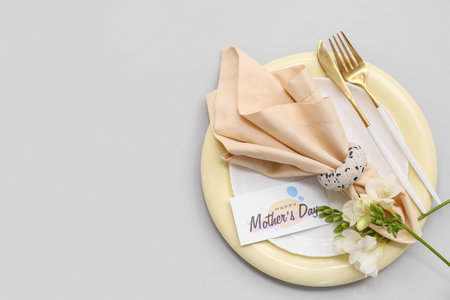 Stylish table setting with greeting card and beautiful flowers on gray background. Mother's Day celebrationの写真素材