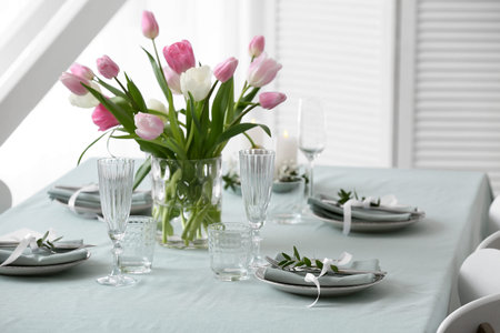 Beautiful table setting for Mother's Day celebration and vase with tulip flowers in dining room