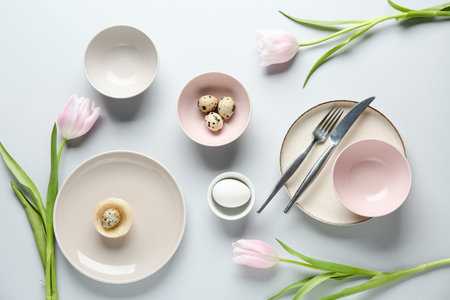 Different clean plates with Easter eggs and beautiful tulip flowers on gray background