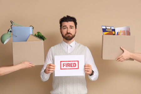 Fired young man and hands with boxes of personal stuff on beige backgroundの写真素材