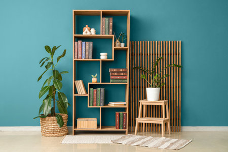 Shelving unit with books, houseplants and screen near blue wall in roomの写真素材