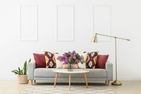 Interior of light living room with sofa, lamp and lilac flowers in vase