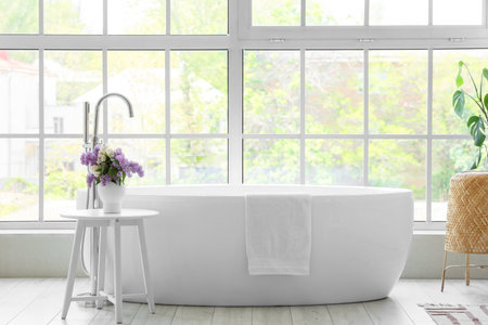 Vase with lilac flowers on table near bathtub in roomの写真素材