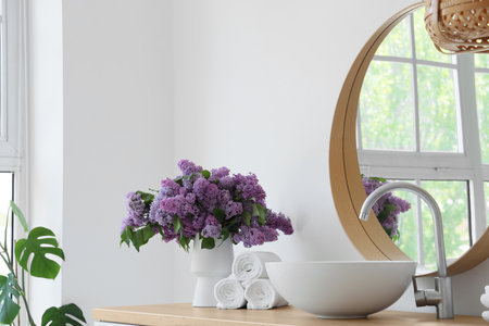 Vase with lilac flowers, towels and sink on table in bathroomの写真素材