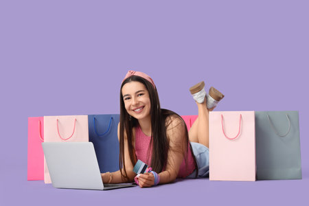 Happy young woman with credit card and laptop shopping online on lilac backgroundの写真素材