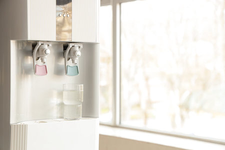 Water cooler with glass near window in office, closeup
