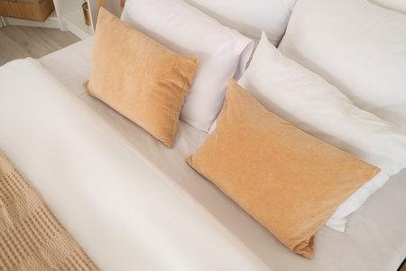 Cozy bed with soft pillows and beige blanket in light bedroom, closeup