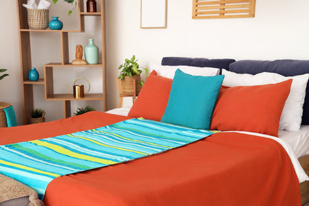 Cozy bed with soft pillows and colorful blankets in stylish bedroom