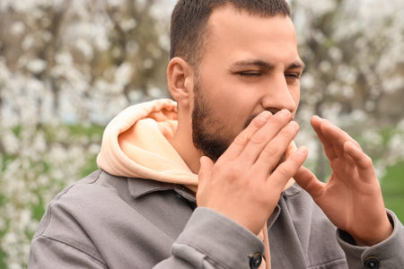 Sick young man suffering from allergy outdoors, closeup