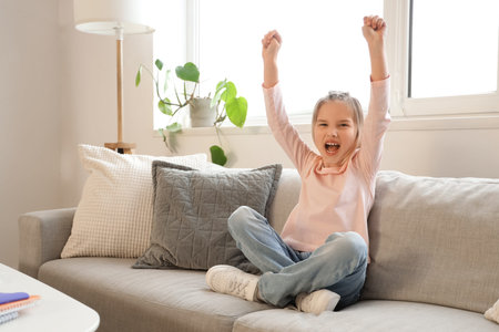 Happy little girl sitting on sofa at homeの写真素材