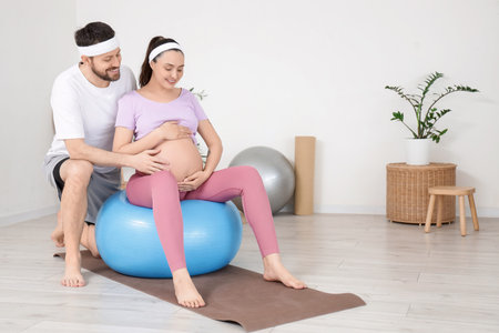 Sporty pregnant couple training on fitball at gym