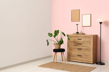 Wooden chest of drawers with lamps and houseplant near pink wall in roomの写真素材
