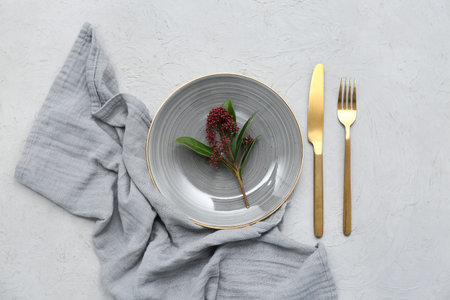 Beautiful table setting with golden cutlery and skimmia japonica plant on gray background