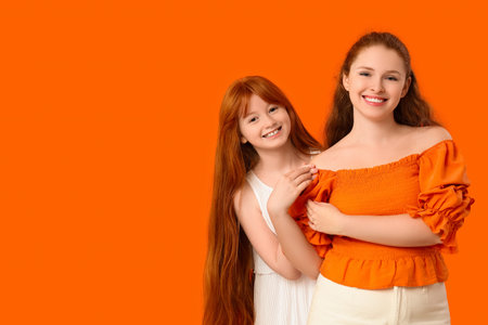 Young ginger woman and her cute daughter on orange backgroundの写真素材
