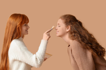 Cute ginger girl applying makeup to her mother on beige backgroundの写真素材
