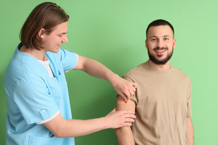 Doctor applying medical patch on man's arm against green background. Immunization conceptの写真素材
