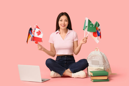 Female Asian student with flags of different countries, books and laptop on pink backgroundの写真素材