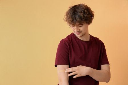 Young man with applied medical patch on beige background. Vaccination conceptの写真素材