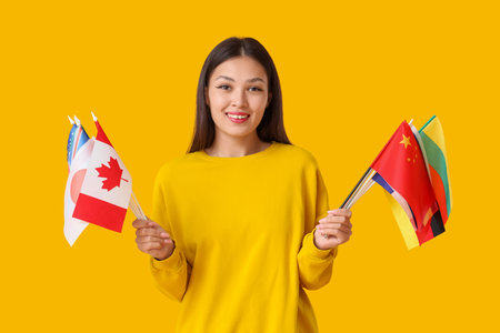 Young Asian woman with flags of different countries on yellow backgroundの写真素材