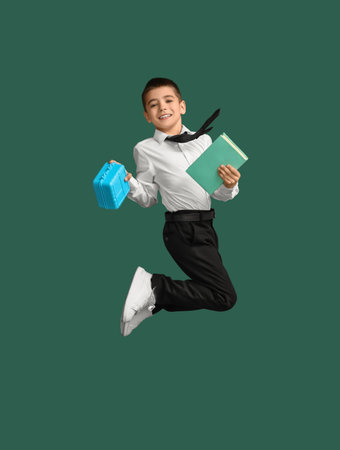 Little schoolboy with lunchbox and book jumping on green backgroundの写真素材